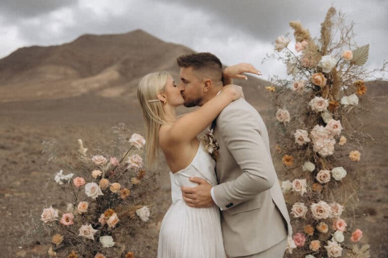 Hochzeitspaar bei Mikro Wedding, umgeben von Blumen, in einer Wüstenlandschaft.