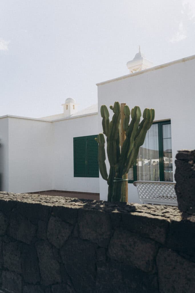 Veronika Haas steht entspannt am Strand von Lanzarote, umgeben von weißen Gebäuden und Cactus.
