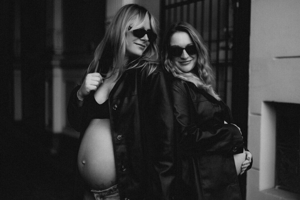 Schwangere Frau mit Freundin bei Babybauch-Fotoshooting, beide tragen Sonnenbrillen.